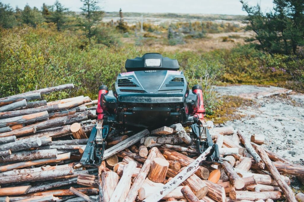 Yamaha snowmobile parked on a pile of cut logs in backcountry terrain